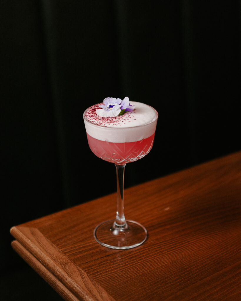 a glass with pink liquid and a flower on top